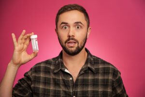 Noam Tomaschoff standing before a pink background with a surprised expression, holding a DNA testing vial